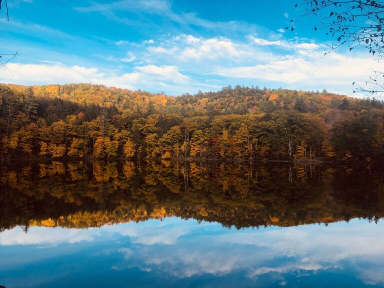 Beautiful autumn foliage reflected in a tranquil lake with a clear blue sky in Vermont