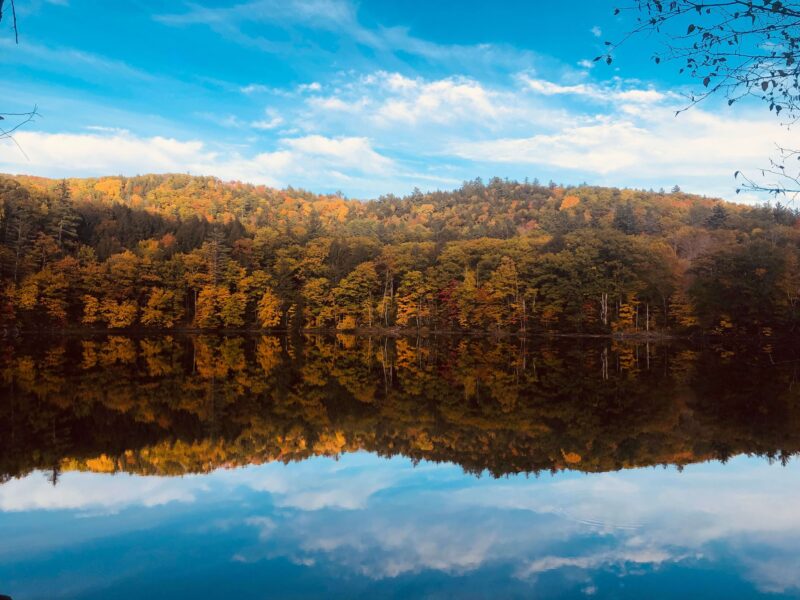 Beautiful autumn foliage reflected in a tranquil lake with a clear blue sky in Vermont