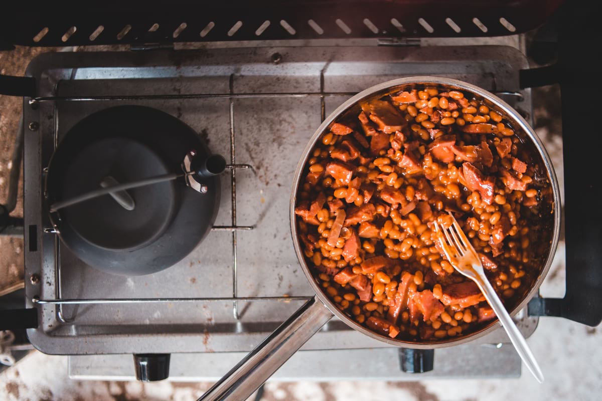 Delicious baked beans and sausage simmering on a stove in a stainless steel pan.